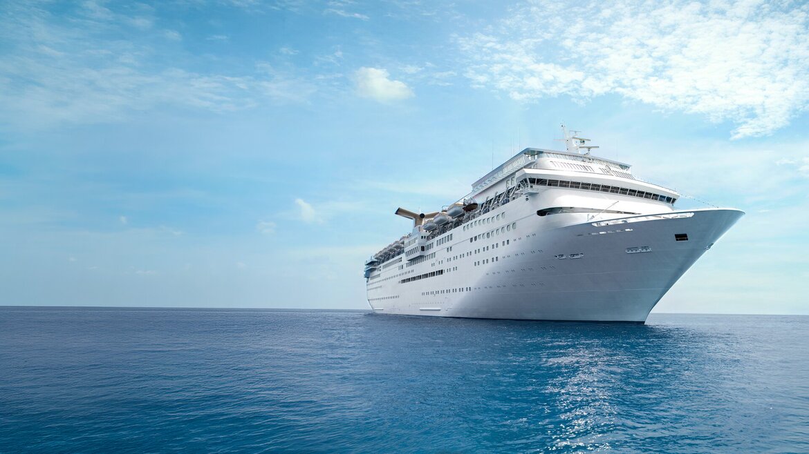 Ein großes weißes Kreuzfahrtschiff gleitet unter einem teilweise bewölkten Himmel über das ruhige blaue Meer.
